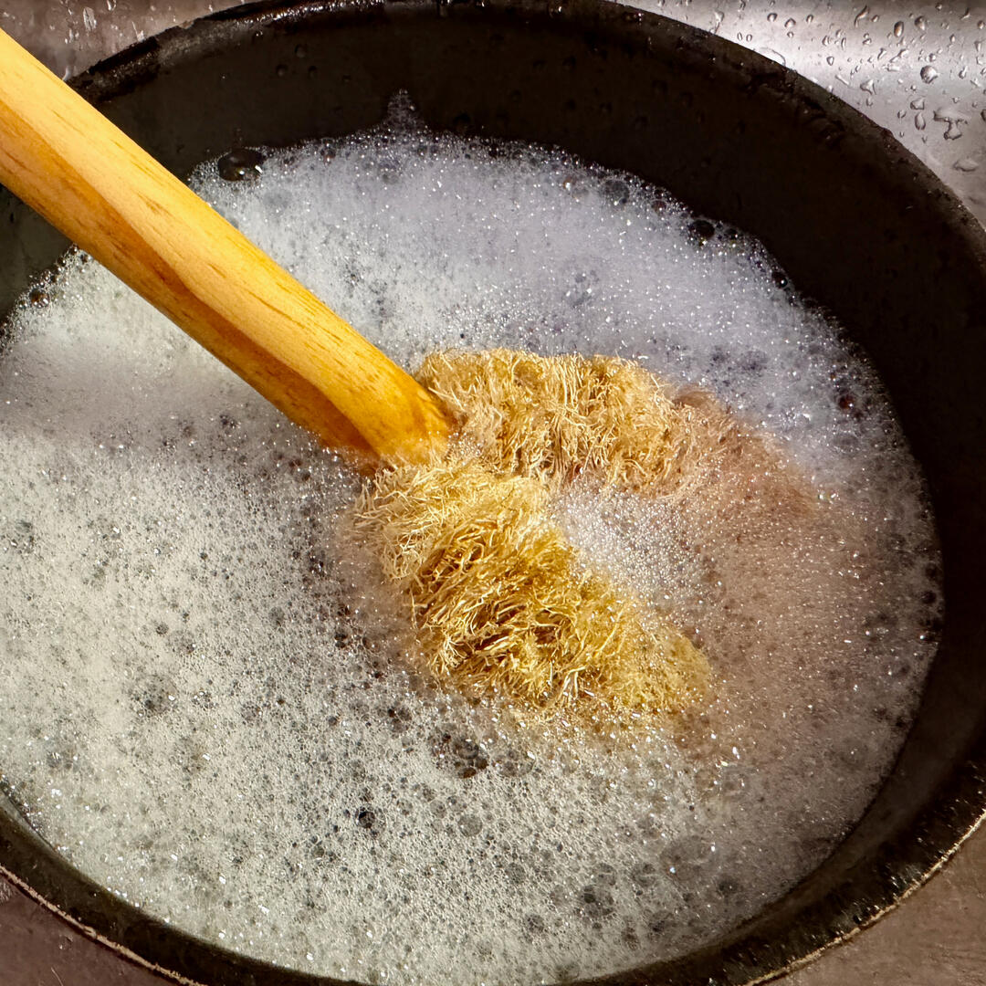 A loofah scrubber inside a pan with soapy water